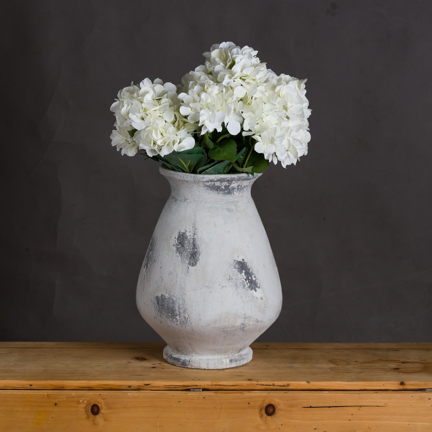 White vase with white flowers on a wooden surface against a dark background