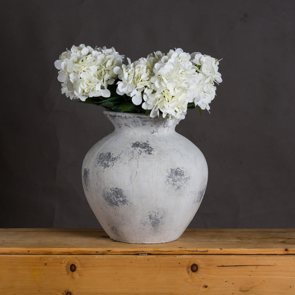 White vase with white flowers on a wooden surface against a dark background
