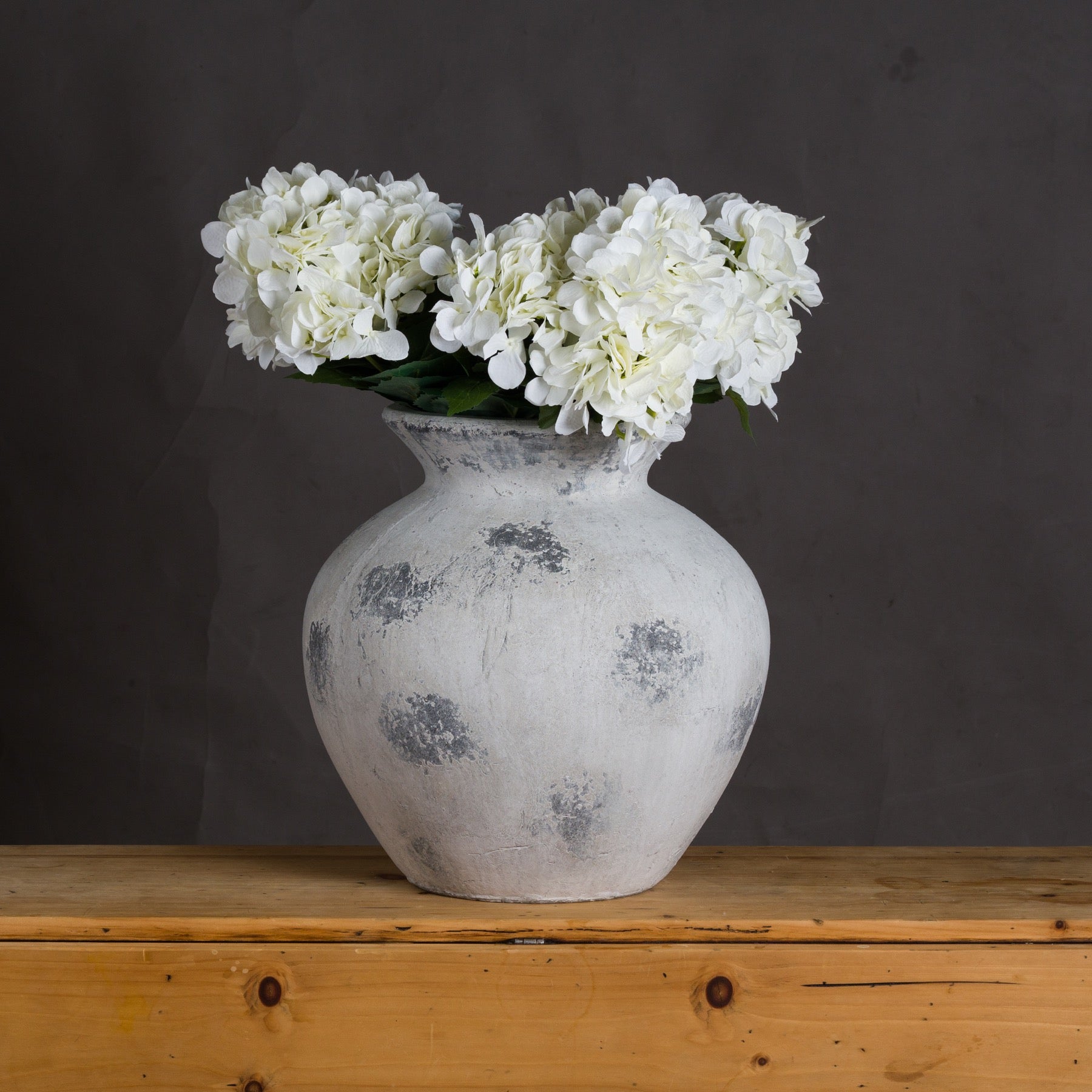 White vase with white flowers on a wooden surface against a dark background