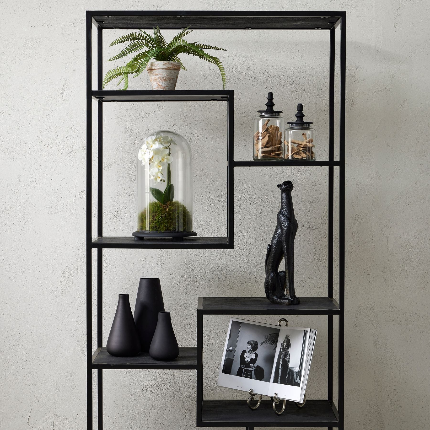Black metal shelving unit with decorative items against a light gray wall