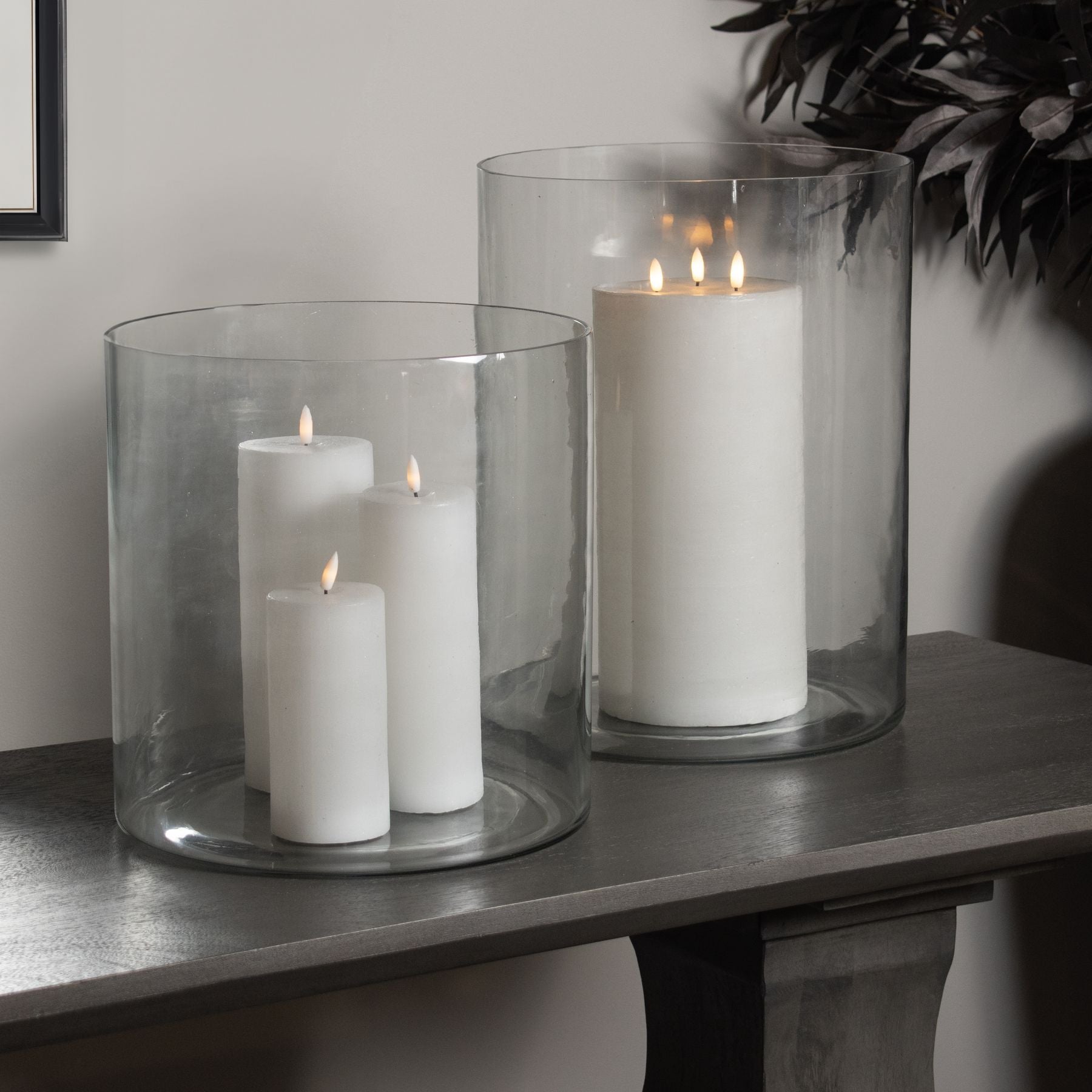 White candles in glass holders on a wooden surface with a neutral background
