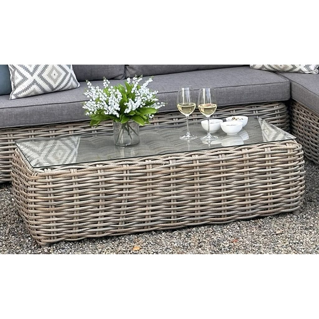 Outdoor patio set with wicker coffee table, sofa, and decorative items on a gravel surface.