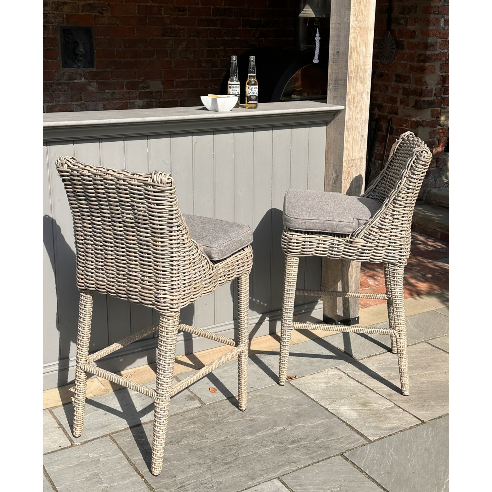 Two wicker bar stools with gray cushions in front of a small outdoor bar.
