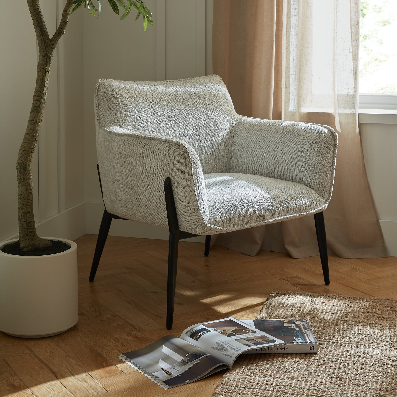 Modern armchair in a room with a plant, open magazine, and curtains.