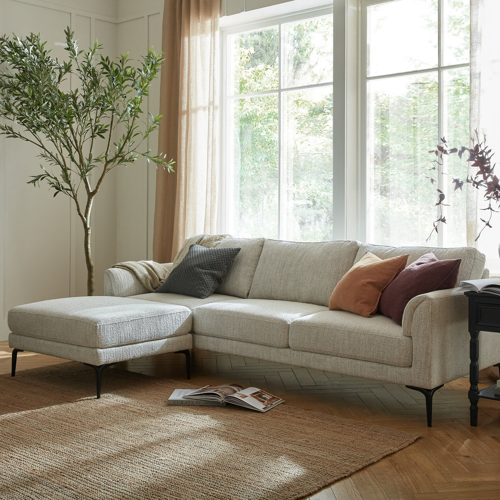 Beige sectional sofa with cushions in a bright living room with large windows.
