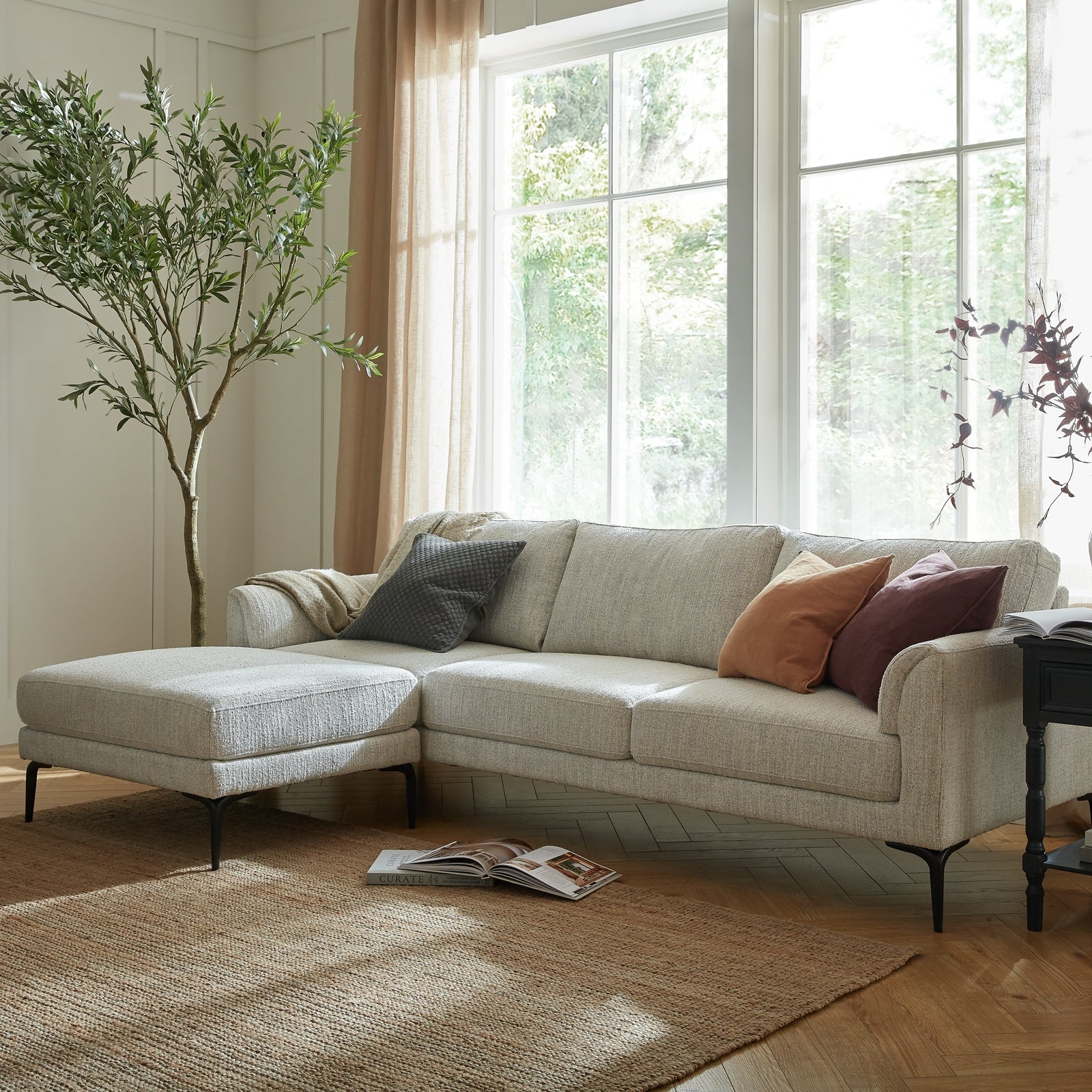 Beige sectional sofa with cushions in a bright living room with large windows.
