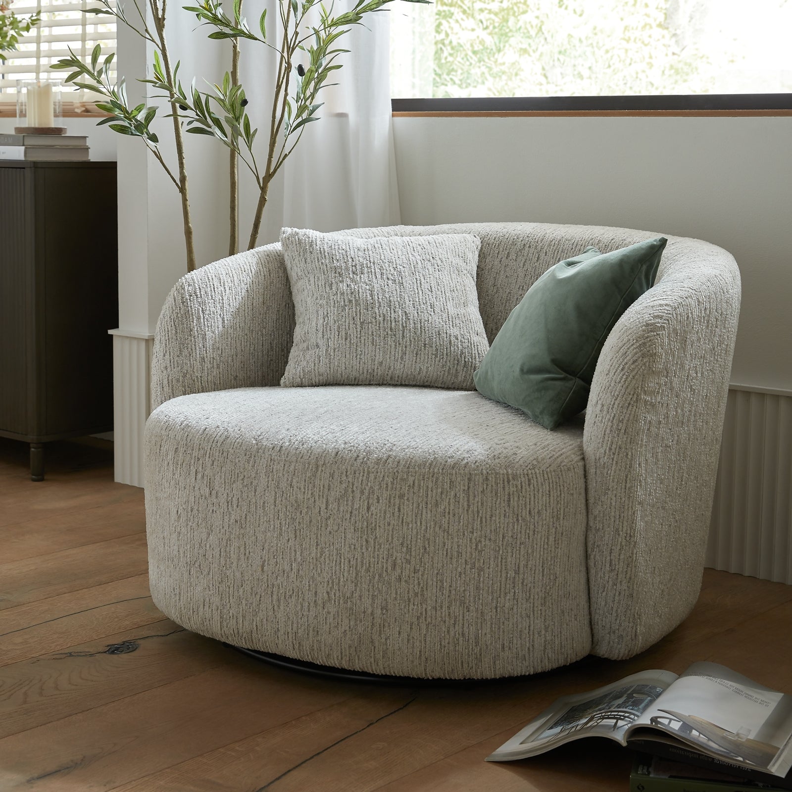 Round beige armchair with cushions in a room with a plant and window.