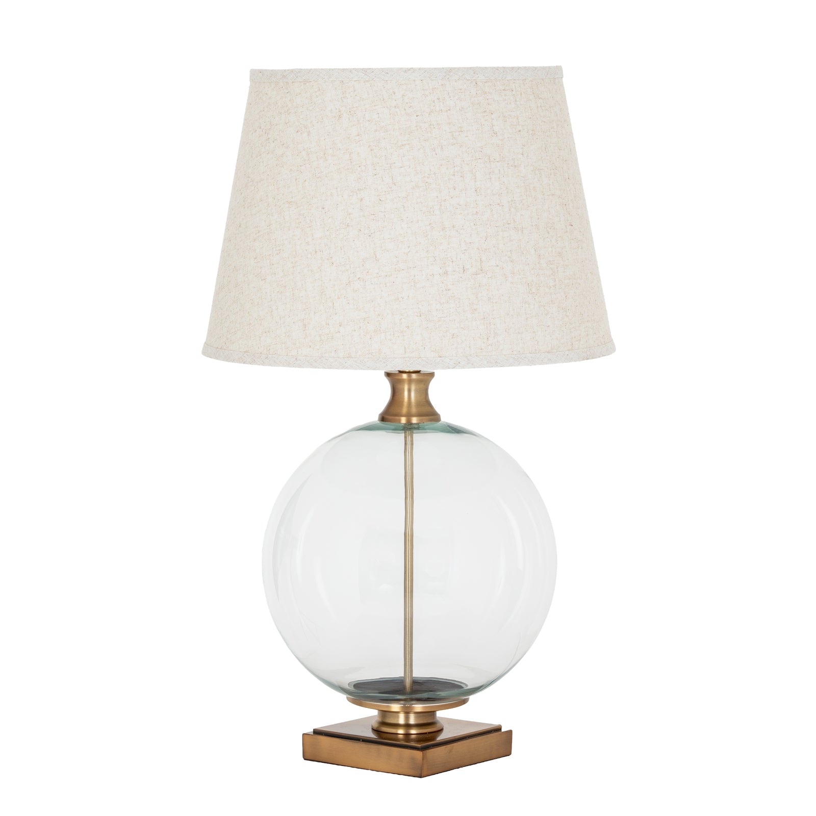 Table lamp with a clear glass base, brass accents, and a beige lampshade on a white background