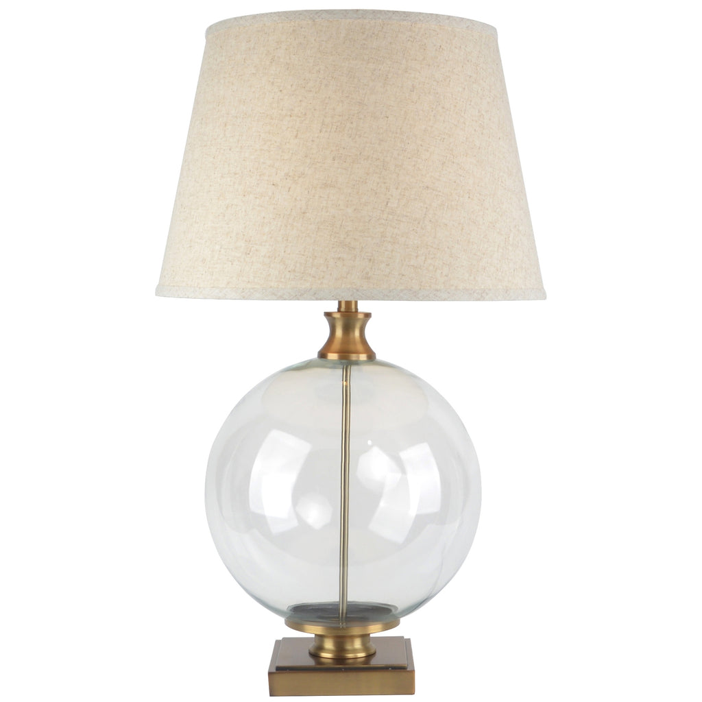 Table lamp with clear glass base, gold accents, and beige fabric shade on a white background