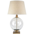 Table lamp with clear glass base, gold accents, and beige fabric shade on a white background